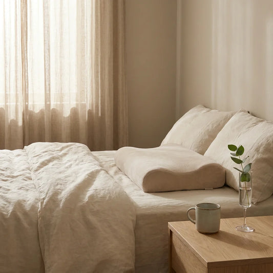 Quiet Luxury wellness scene with an ergonomic neck support pillow on cream-colored linen.